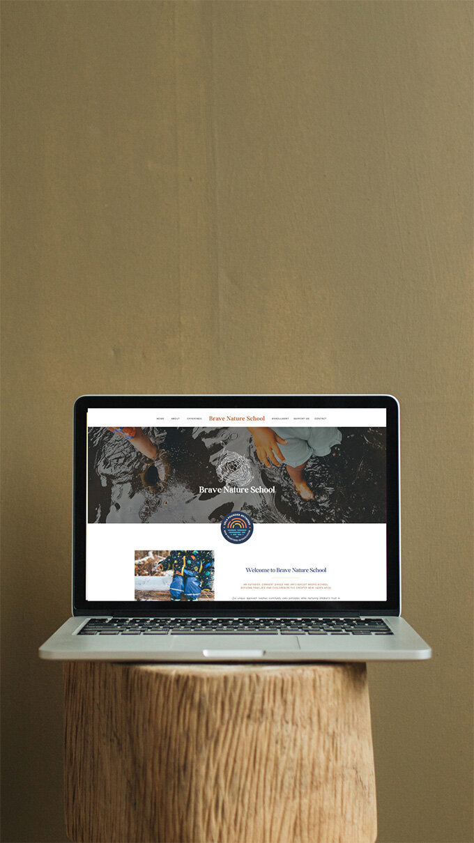 A laptop on a wooden table displaying a photo of a nature preschool setting.