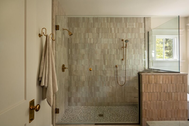 Calm neutral-toned glass-enclosed shower with gold hardware and floor-to-ceiling tile in serene master bathroom.
