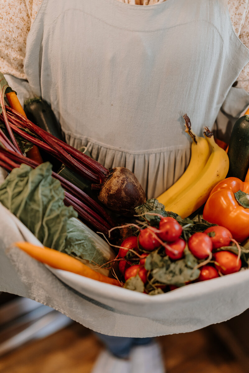 Kenna holding a variety of fruits and veggies in her apron