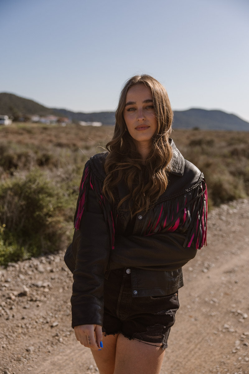 A woman in cowboy jacket is standing in a field and posing for a shoot.