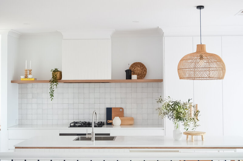 Minimalist kitchen with white cabinets, wooden accents, a woven pendant light, and green plant decor, all crafted by a full-service interior design team in Newcastle.