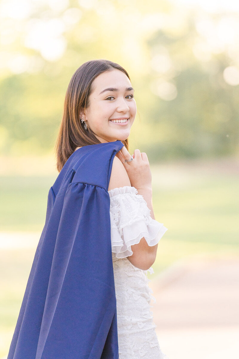 high school girl holding graduation gown looking back taken by senior photographer in Ashburn, Virginia