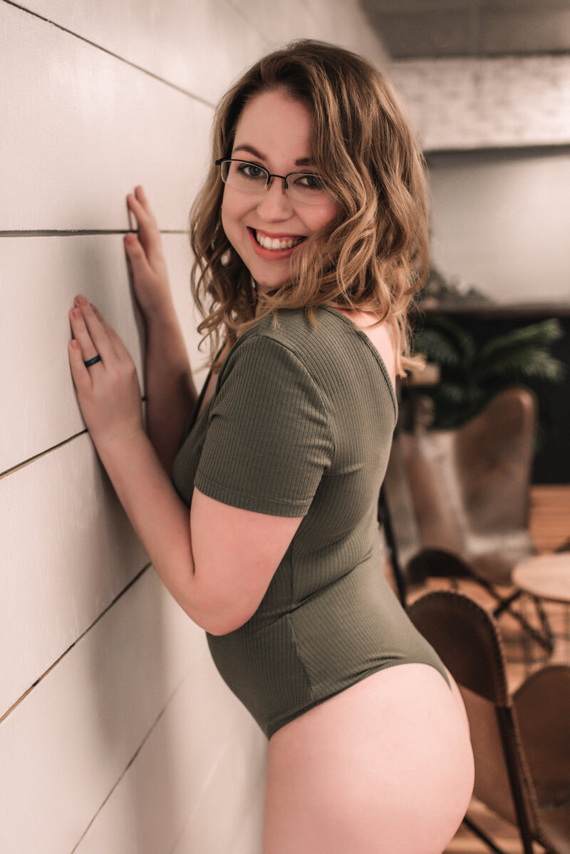Danielle, owner of The Haven Studio kneeling down against the wall wearing a olive green bodysuit