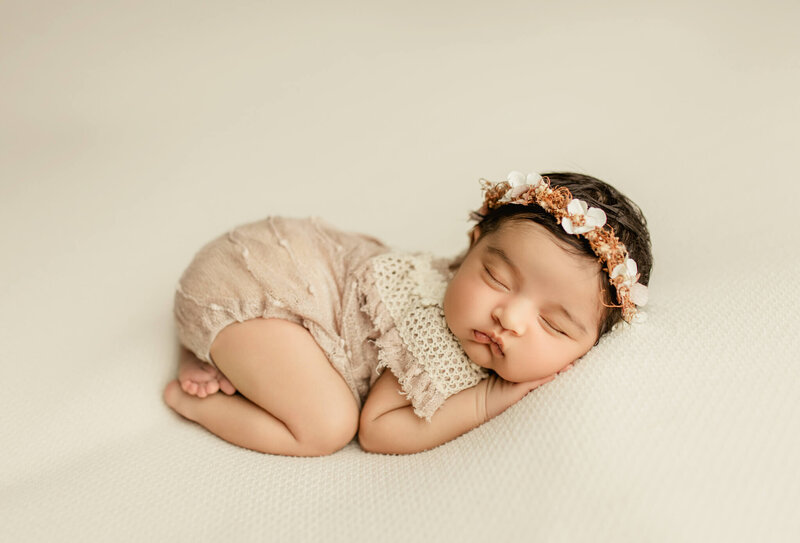 Newborn baby wearing a simple floral headband, asleep on a textured blanket, photographed in an elegant fine-art style.