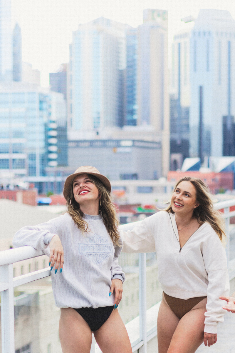An image of two young women in bathing suits laughing and smiling on a roof top in an urban setting.