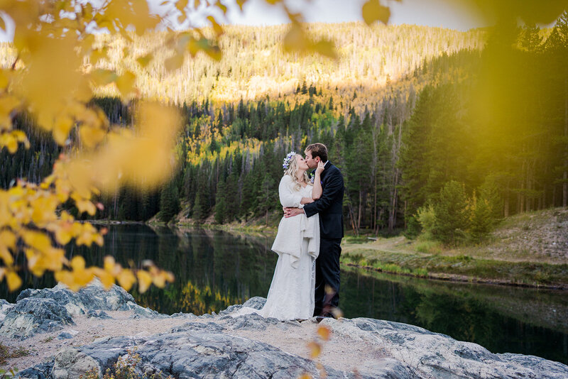 A couple stands with their two small children and officiant next to a lake and mountains