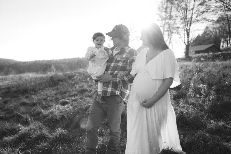 husband, pregnant wife and daughterwalking in a field together during maternity session