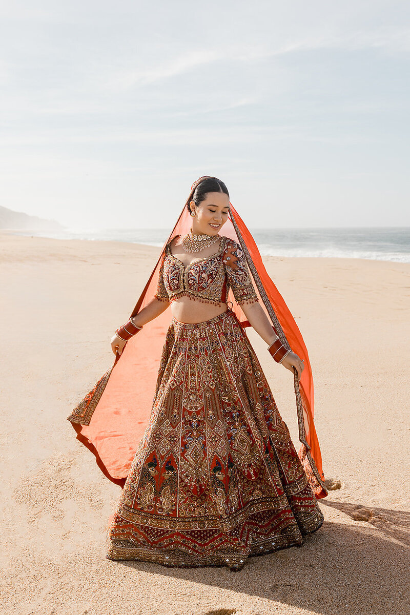 Bride wearing colorful Indian dress on beach with sand