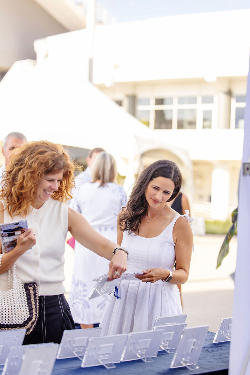 Two women outdoors smiling and looking at papers during an event.