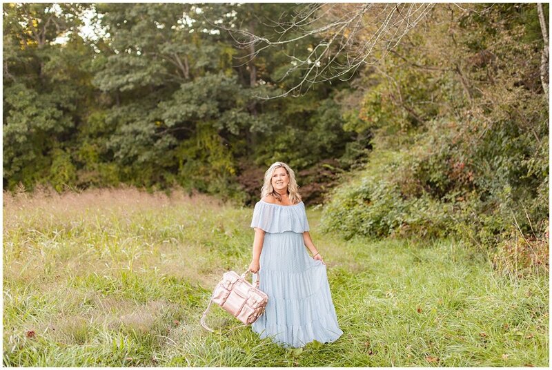 photographer standing in field with gold camera bag and blue flowy dress in Asheville, North Carolina
