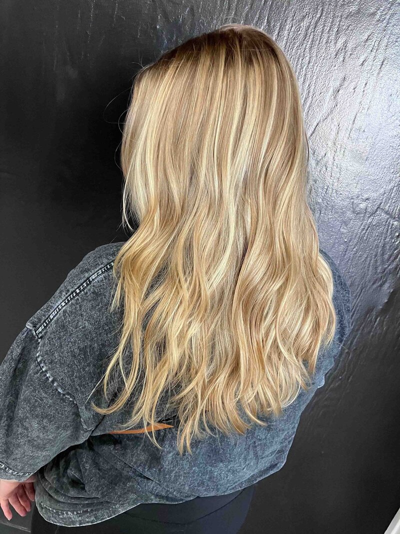 A girl with blonde highlights facing a black wall