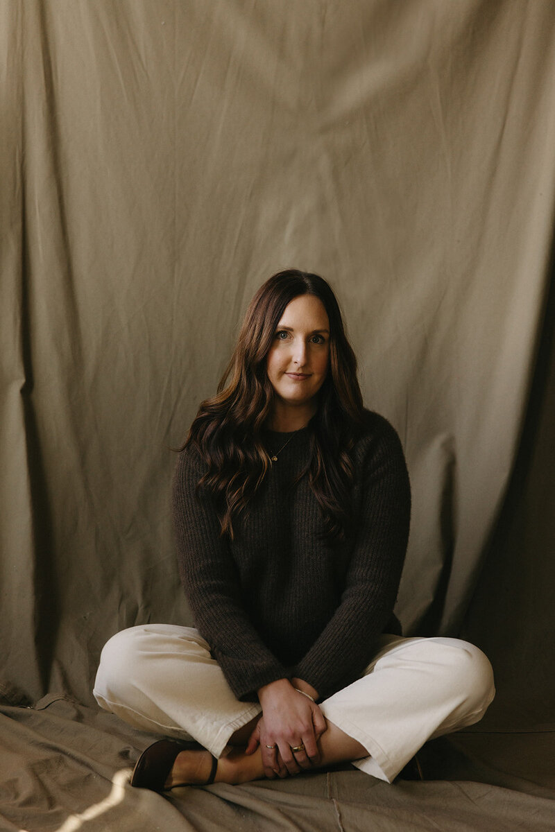Portrait of the Gatherie Creative founder seated cross-legged against a draped olive backdrop, conveying her approachable brand design expertise.