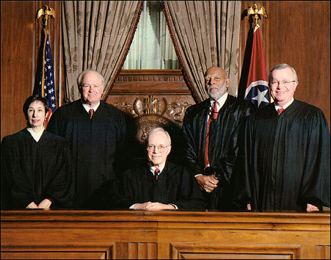 Group portrait of five Tennessee Supreme Court justices in formal judicial robes, posed in a courtroom setting with American and Tennessee state flags in the background.