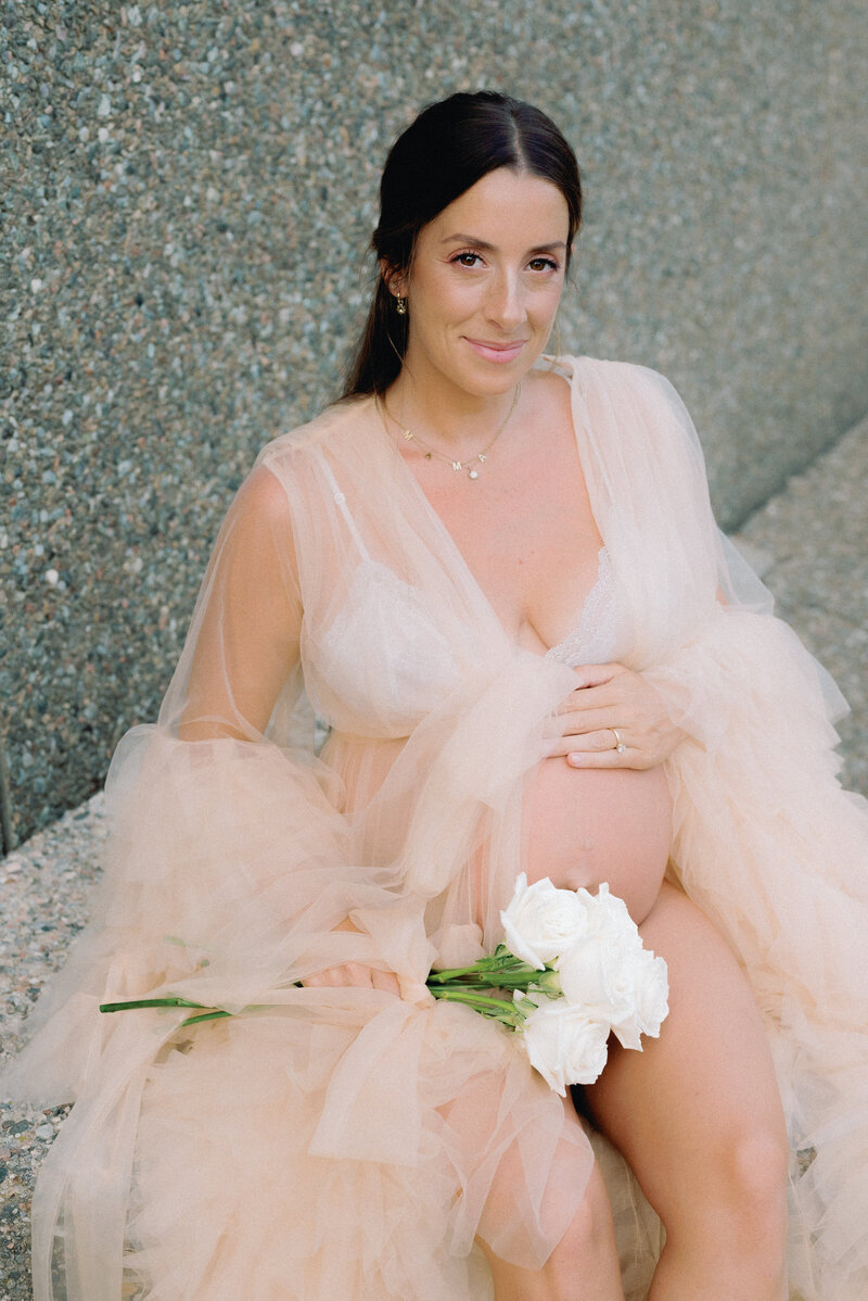 Expecting mother in maternity gown holding belly and flowers