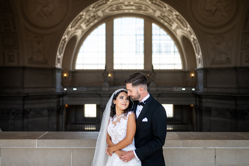 Bride and groom in San Francisco City Hall rotunda with ornate arched windows - wedding photographer