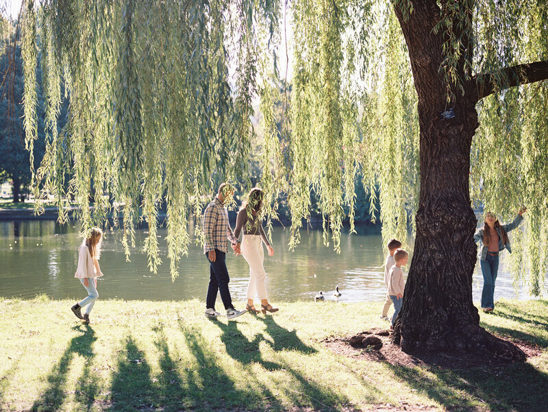 Glowy photo of a family of 6 walking under a tree beside a pond