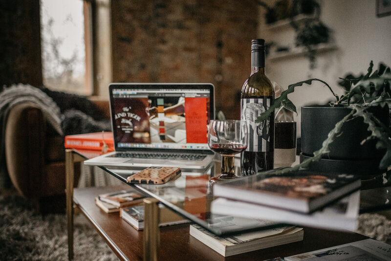 A coffee table with a luxury branding project on Clair Schwem's computer in the background. A casely phone case sits in front of a bottle of red wine.