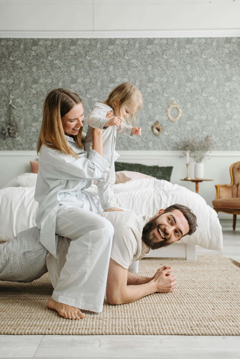 Mother and toddler sat on father's lap in bedroom