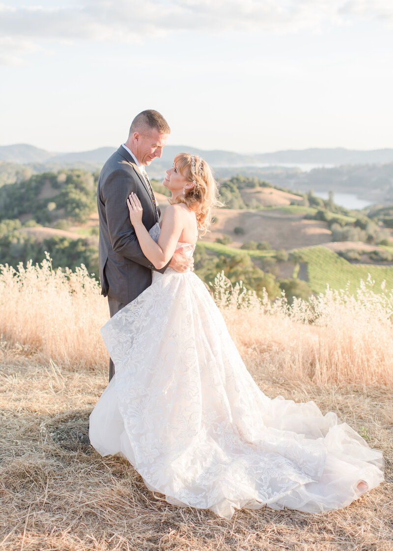 wedding couple holding each other on top of hill in the valley. 