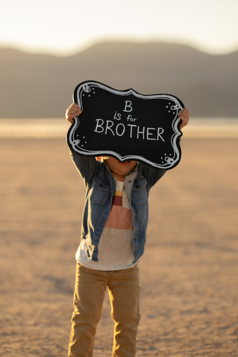 young boy holding a sign announcing his little brother at a family session with las vegas portrait photographer alexis dean