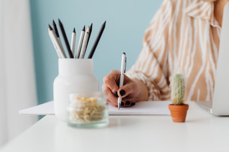 woman writing in a notebook pens in a cup