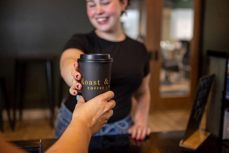 smiling woman reaching for coffee cup from across the counter. 