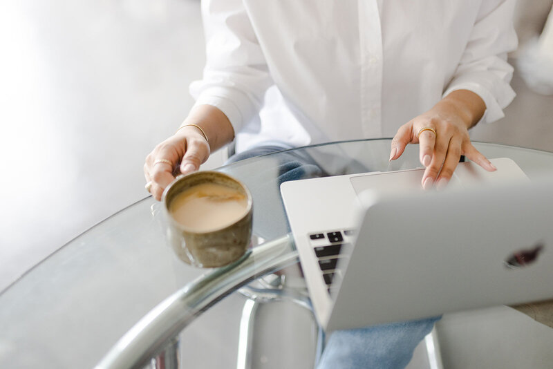 Female entrepreneur sits in front of laptop with a cup of coffee in hand