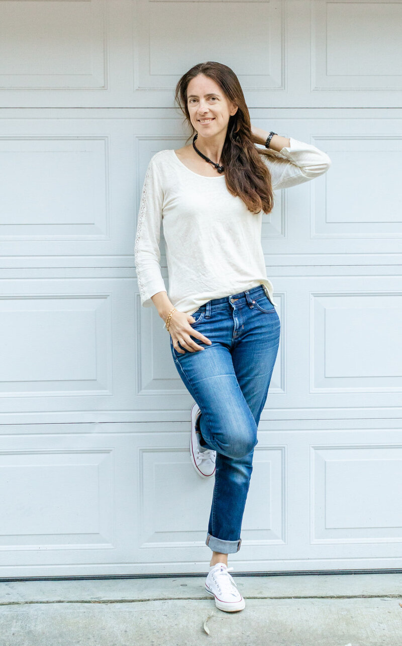 woman in casual outfit jeans and white top standing one hand in pocket one hand in hair