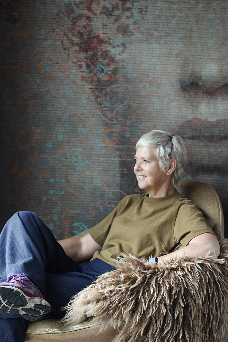 Threa van LOOSZ Interieur & Styling zittend in een comfortabele stoel, met een unieke artistieke muurprint als achtergrond die warmte en karakter toevoegt.