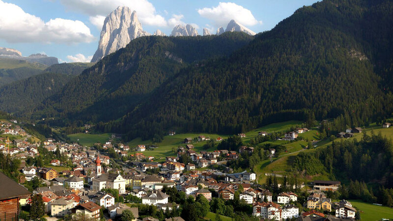 Val Gardena with houses all through the valley and a huge mountain looming over the whole town