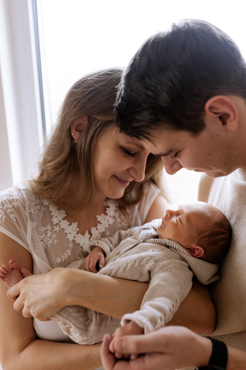 Mutter und Vater halten Baby auf dem Arm und laecheln es an