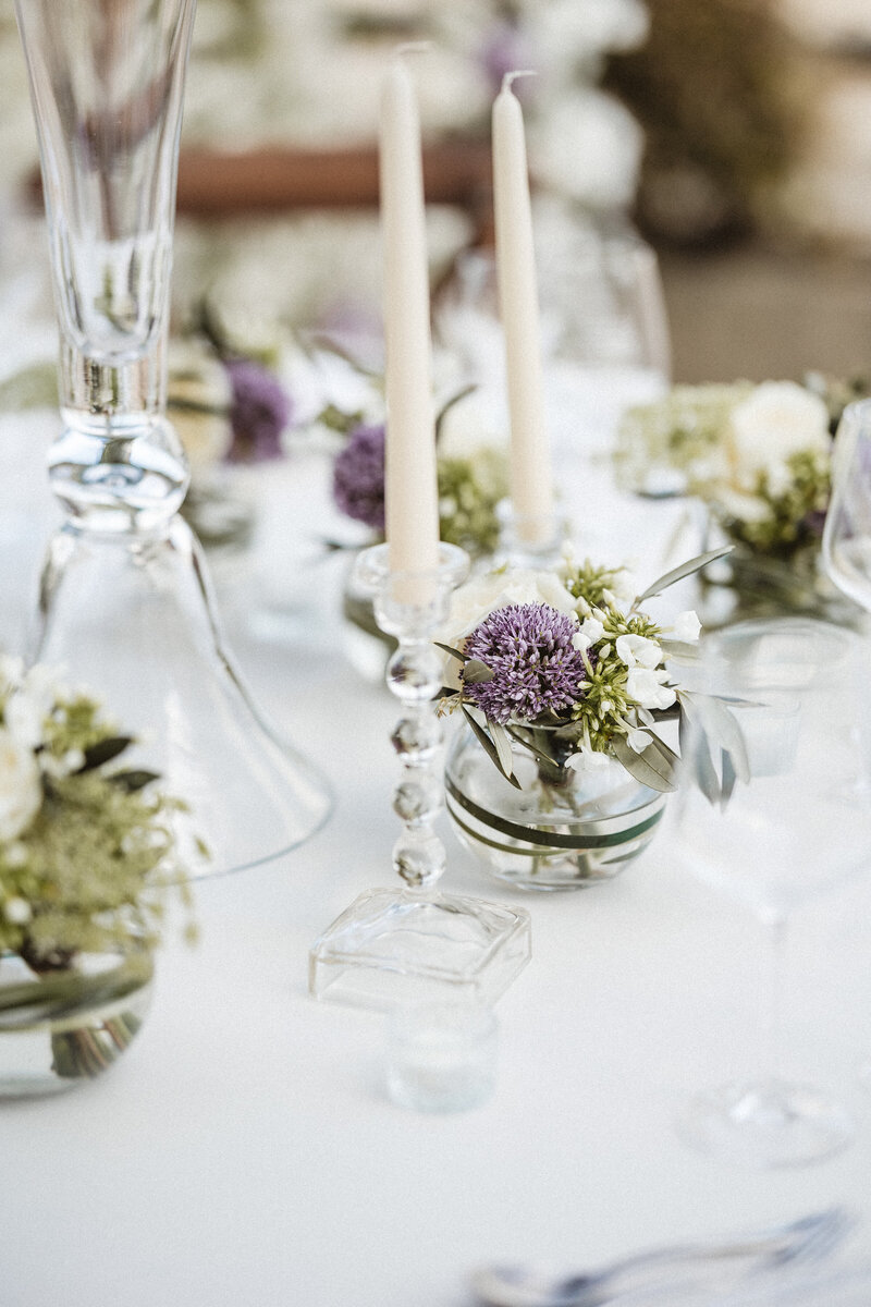 Low globes of flowers including alliums paired with glass candle holders and white tapered candles