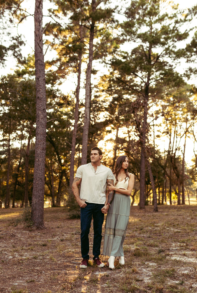 young married couple stand holding each others arm backlit by golden sunset light during couples portrait session