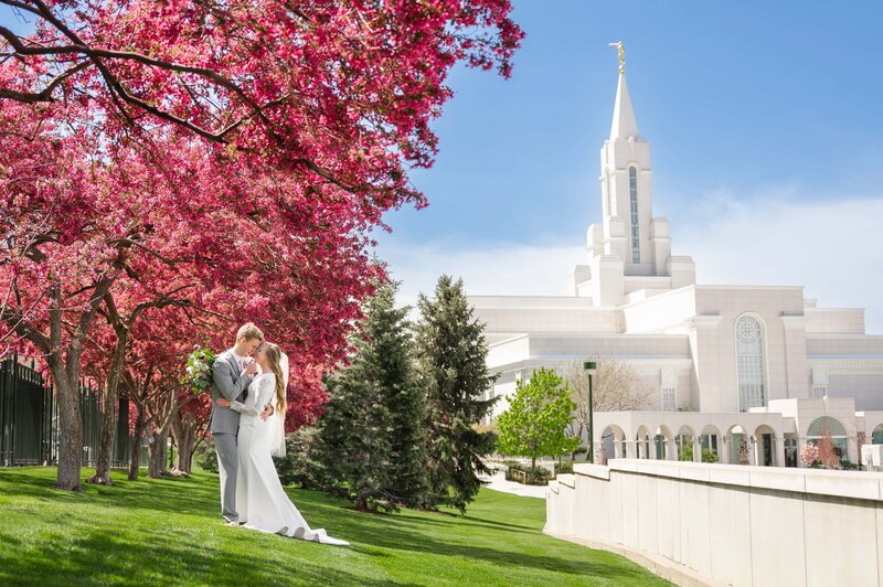 Bride and groom holding each other close in front of the Bountiful temple during their spring wedding.
