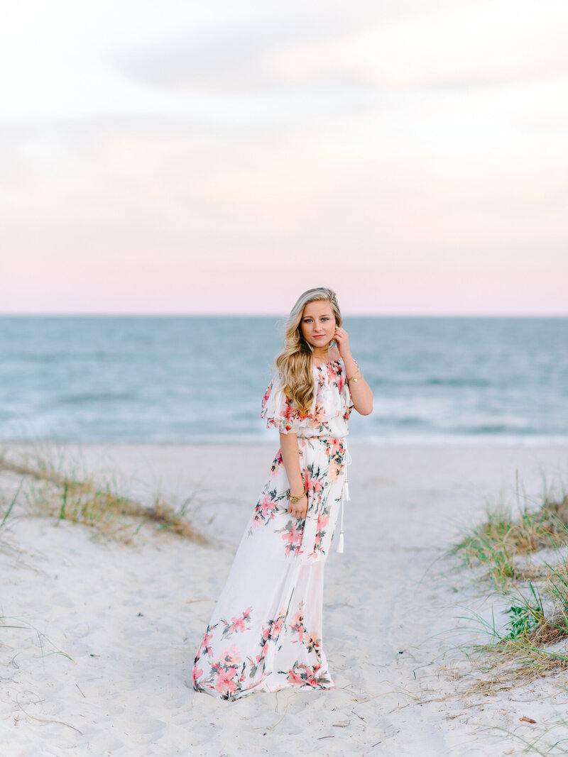 High school senior girl in floral dress standing on beach dunes during sunset in Charleston, South Carolina