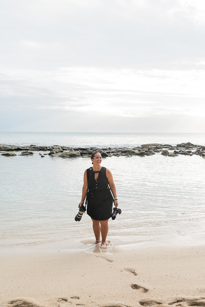 Jess Collins standing on a beach holding her cameras