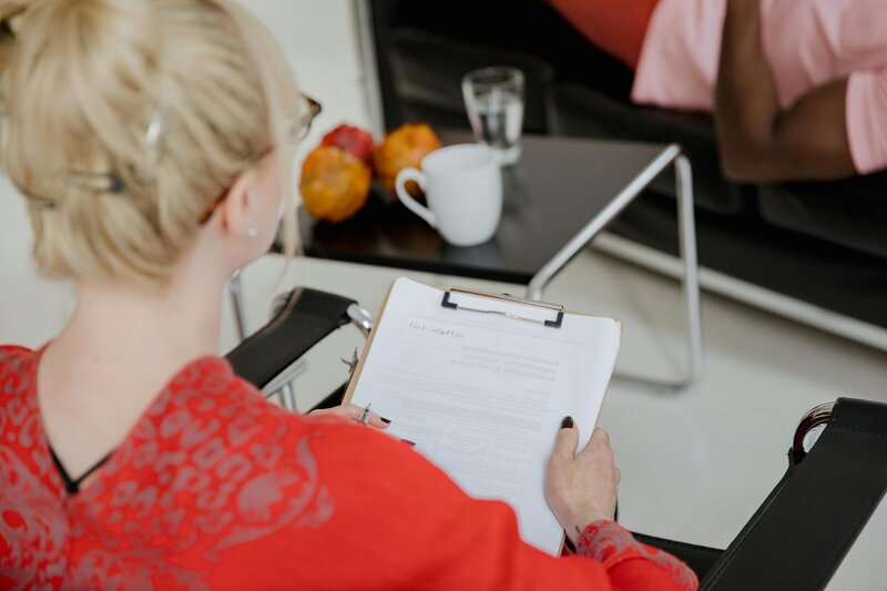 Woman in a red shirt with a clipboard. Appears she is helping a client.