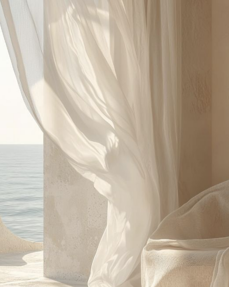 Elegant sheer curtains flowing beside a cozy armchair with ocean view in a serene, sunlit space