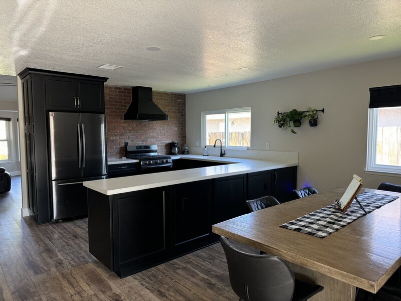 A newly remodeled kitchen with black cabinets, white counter tops, and a focal wall with red brick for an industrial style kitchen.