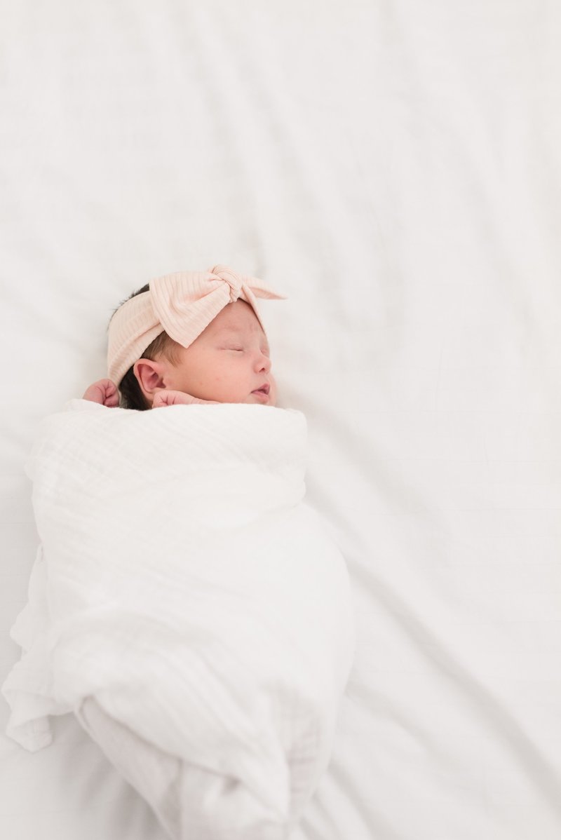 Newborn baby girl swaddled in a white blanket with a pink bow on her head for a Nashville newborn picture