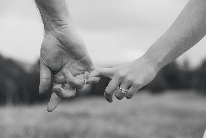 Black and white photo of couple holding hands showing the ring at their Colorado mountain engagement session