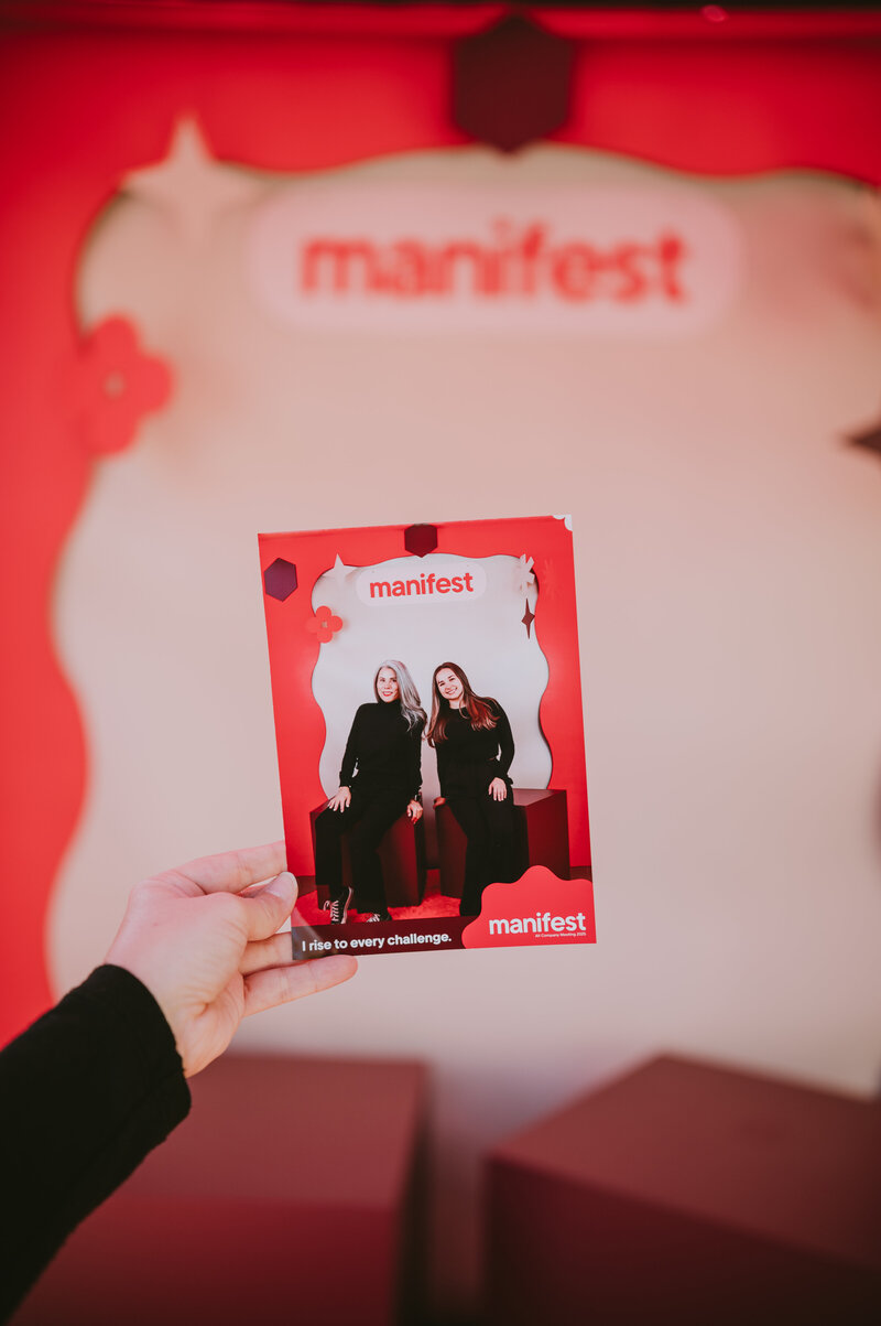 Hand holding a branded MISGIF photo booth printout in front of a pink “Manifest” event backdrop, highlighting customized photo experiences for corporate events in Phoenix, Arizona