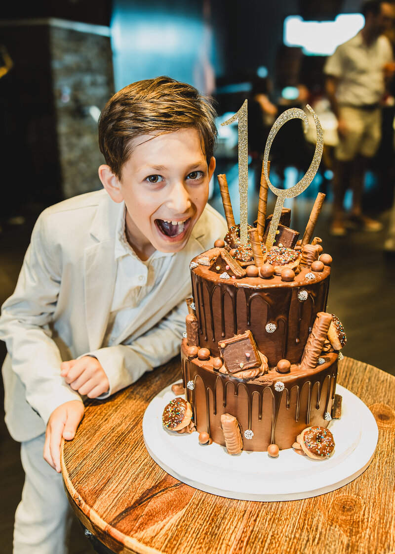 Boy jokingly about to face-plant into a birthday cake at an upscale birthday party
