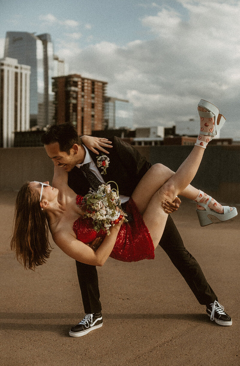 man holding girl in red sequin dress bridal style on a parking garage 