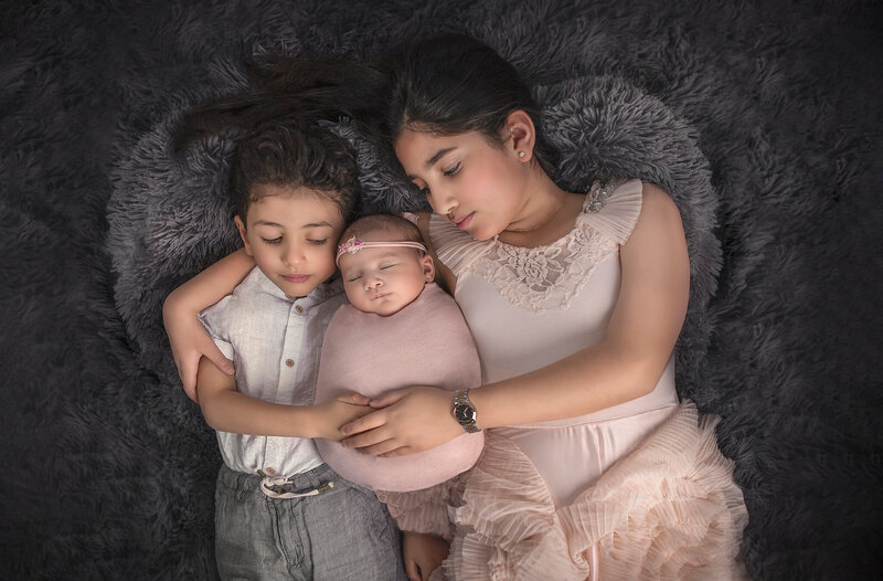 Big brother and sister lovingly cuddling their newborn sibling on the floor, captured in a heartwarming family portrait during a fine art photography session in Ottawa."