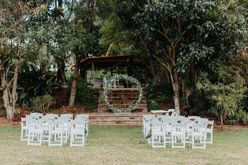 Wedding ceremony arch on steps in a garden with white ceremony chairs