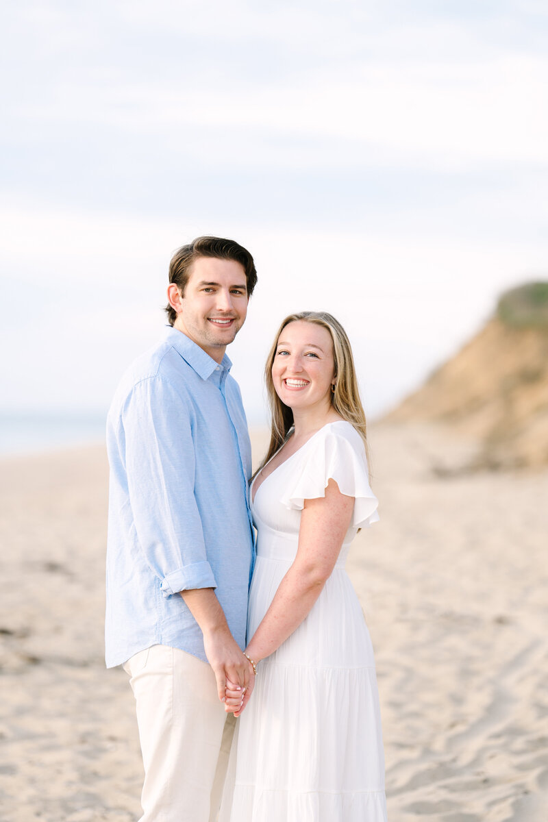 couple holding hands smiling at the camera during their sunrise nauset light beach engagement session