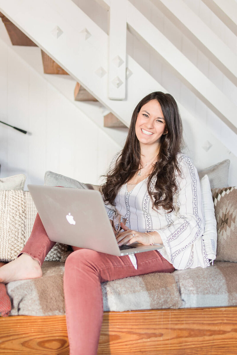 Find Your Freedom Co. founder Laura sitting on a couch in a  cabin working on her laptop