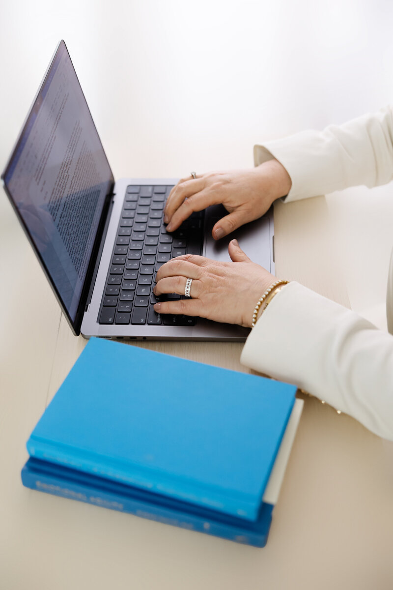 Hands typing on laptop beside blue books symbolizing leadership coaching and focus