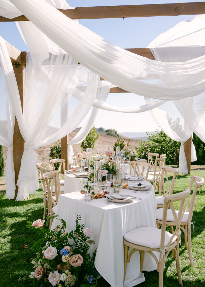 An intimate black-and-white wedding moment at the Royal Palms in Scottsdale, Arizona. The bride, elegantly dressed in lace, sips champagne while her groom drapes his jacket over her shoulders, capturing a timeless and romantic celebration.